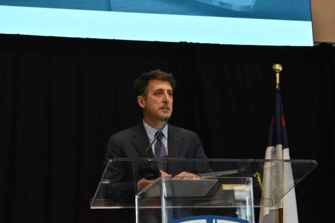 Dr. Andrew Abela speaking at a podium. 