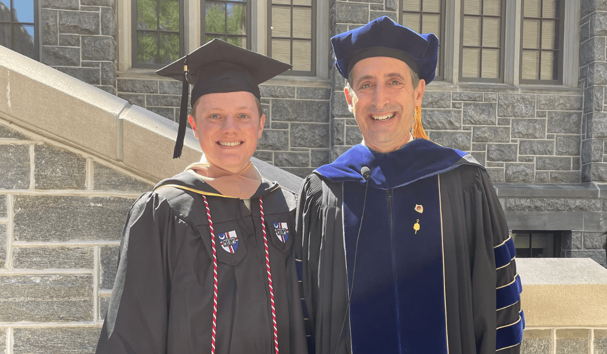 Photo of Grady J Connolly standing in front of Maloney Hall on his graduation day. He is standing next to a professor in academic regalia.
